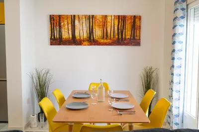 a dining room table with yellow chairs and a painting on the wall at Piso San Roque in Sanlúcar de Barrameda