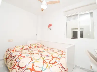 a white bedroom with a bed with a colorful blanket at Piso San Roque in Sanlúcar de Barrameda