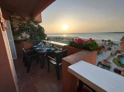 a balcony with a table and chairs and the beach at Ático Reig frente al mar in Sanlúcar de Barrameda