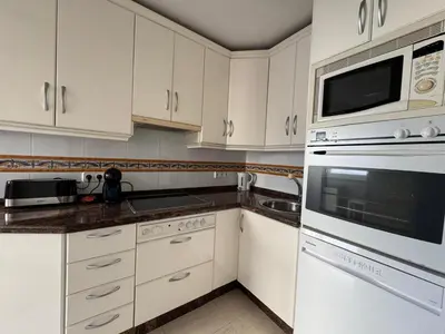 a white kitchen with white cabinets and a microwave at Aires de Regla, Apartamentos Living Sur in Chipiona
