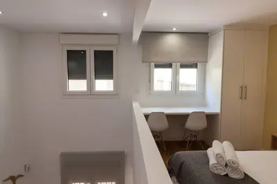 a white bedroom with a bed and two windows at El Duplex de Barrocal in Cádiz