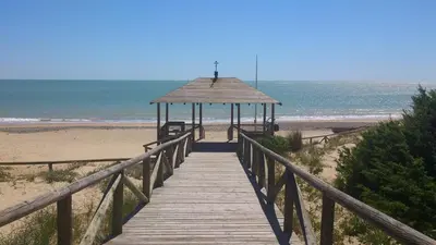 a wooden boardwalk leading to a beach with a gazebo at Casa Reyes in Rota