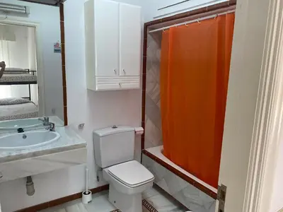 a bathroom with a toilet and an orange shower curtain at Apartamento terraza puerto sherry. in El Puerto de Santa María