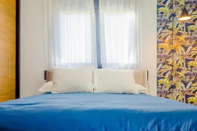 a bed with blue sheets and white pillows and a window at Villa Minerva in Chiclana de la Frontera