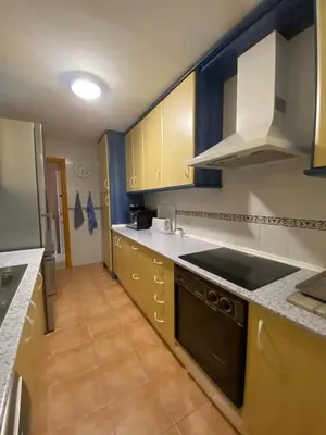 a kitchen with yellow cabinets and a black stove at Apartamento Costa de la Luz - Parking y Terraza in Chipiona