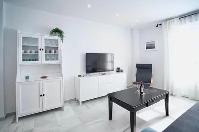 a white living room with a tv and a table at Apartamento Montefillo in Sanlúcar de Barrameda