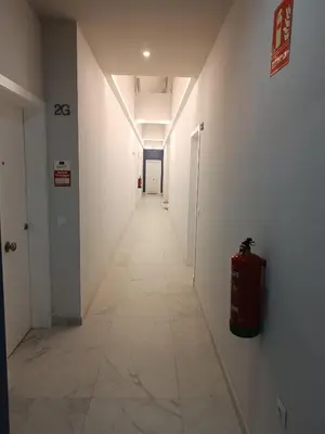 a hallway with white walls and a long hallway with a fire extinguisher at APARTAMENTO LUPA in Cádiz
