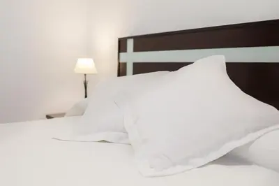 a white bed with white pillows and a lamp at Casa Sumariva in Sanlúcar de Barrameda