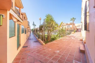 a brick walkway between two buildings with palm trees at APARTAMENTO EN URBANIZACIÓN AL-ÁNDALUs CERCA DE LA PLAYA DE LA BARROSA in Chiclana de la Frontera