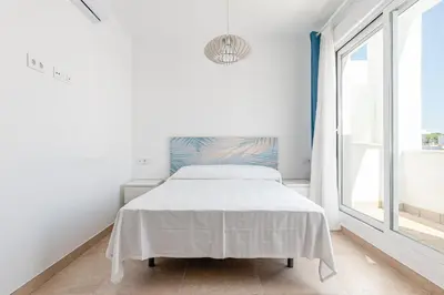a white bedroom with a bed and a window at Casa Playa Andres in Conil de la Frontera