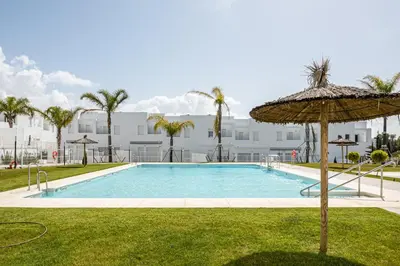 a swimming pool with an umbrella and a building at Casa Playa Andres in Conil de la Frontera