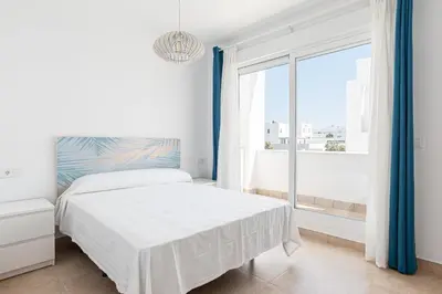a white bedroom with a bed and a large window at Casa Playa Andres in Conil de la Frontera