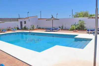 a swimming pool with chairs and an umbrella at Chalet La Florida in Conil de la Frontera