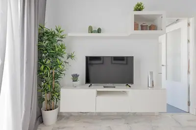 a white living room with a tv on a white wall at Jerez Paralejo Ha Apartment in Jerez de la Frontera