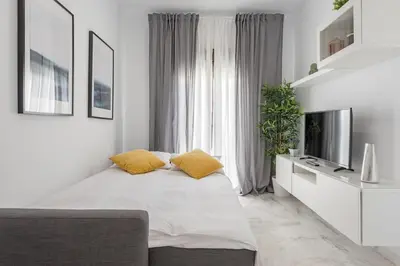 a white bedroom with a bed with yellow pillows at Jerez Paralejo Ha Apartment in Jerez de la Frontera