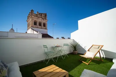 a balcony with chairs and a table and a building at El ático de Reyes in Sanlúcar de Barrameda