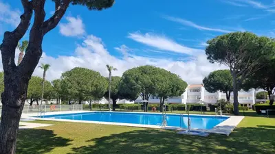 a swimming pool in a park with trees and a building at Apartamento Retama Golf in Chiclana de la Frontera