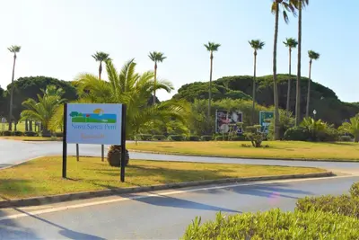 a sign on the side of a road with palm trees at Bonito apartamento con jardín privado en Novo in Novo Sancti Petri