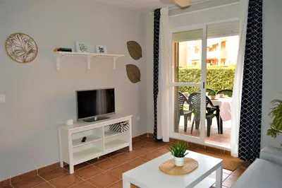 a living room with a tv and a table at Bonito apartamento con jardín privado en Novo in Novo Sancti Petri