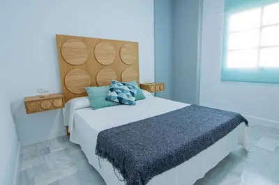 a bedroom with a large bed with a wooden headboard at El Patio del Sol, Apartamentos Living Sur in Sanlúcar de Barrameda