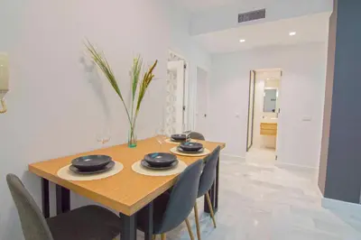 a dining room with a wooden table and chairs at El Patio del Sol, Apartamentos Living Sur in Sanlúcar de Barrameda