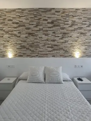 a bedroom with a white bed and a brick wall at Alojamientos La Menúa in Los Badalejos