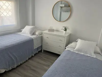 two beds in a room with a mirror and a dresser at Apartamento en Rota con piscina y parking junto al mar in Rota