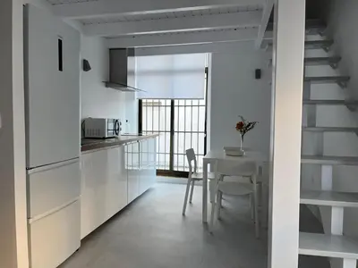 a kitchen with white cabinets and a table with chairs at Loft EL DUQUE in Sanlúcar de Barrameda