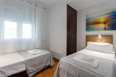 a white bedroom with two beds and a window at El Velero en la playa Victoria Grupo AC Gestion in Cádiz