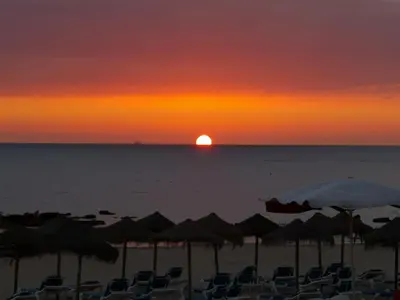a sunset on the beach with chairs and umbrellas at El Velero en la playa Victoria Grupo AC Gestion in Cádiz