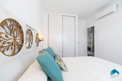 a white bedroom with a white bed and blue pillows at Sauz B in Chiclana de la Frontera