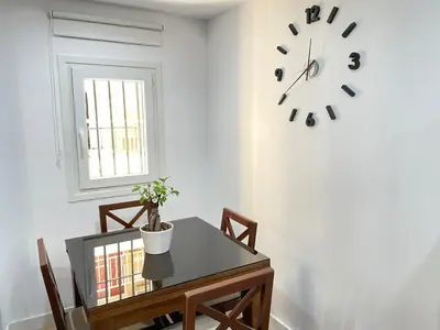 a dining room with a table and a clock on the wall at El pisito Sanlúcar in Sanlúcar de Barrameda