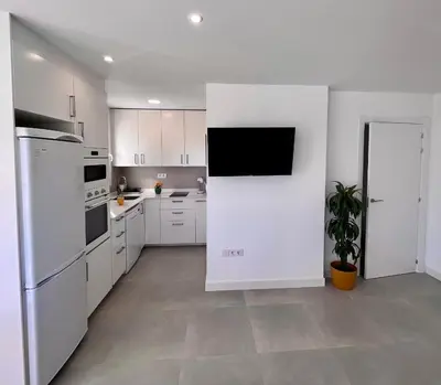 a kitchen with white cabinets and a tv on a wall at GATU Villa Soleá parking, piscina, pistas tenis, playa de Valdelagrana in El Puerto de Santa María