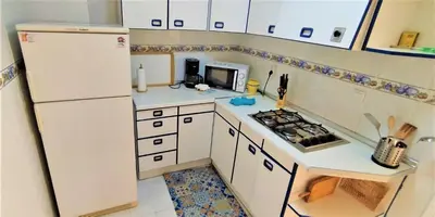 a small kitchen with white cabinets and a refrigerator at Apartamento Tres Carabelas, AC, Wifi, Parking in Sanlúcar de Barrameda