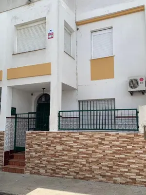 a white building with a black door and a brick wall at Casa Amapola - Costa Bahía de Cádiz in Puerto Real
