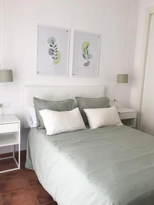 a bedroom with a bed with two white tables and two pictures at Playa Laguna Bajo Parking in Chipiona