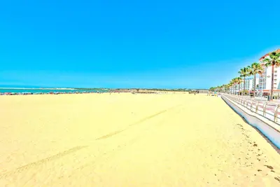 a sandy beach with palm trees and a building at Ocean View Beach Apartment with Pool & Balconies in El Puerto de Santa María