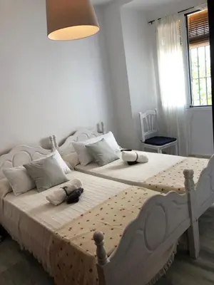 two beds in a white bedroom with a window at ACOGEDOR APARTAMENTO EN SANLUCAR DE BARRAMEDA in Sanlúcar de Barrameda