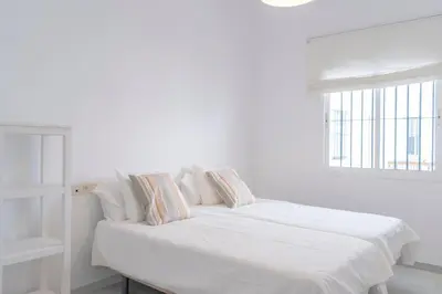 a white bedroom with a bed with pillows and a window at Apartamento completamente nuevo en pleno centro del Puerto in El Puerto de Santa María