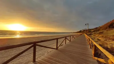 a wooden boardwalk leading to the beach at sunset at Acogedor estudio junto playa, El Manantial in El Puerto de Santa María