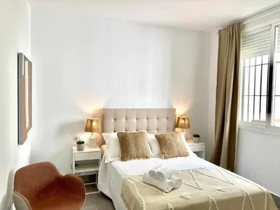 a white bedroom with a large bed and a chair at Apartamentos Casa Macías in Cádiz