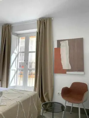 a bedroom with a bed and a window and a chair at Apartamentos Casa Macías in Cádiz