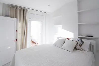 a white bedroom with a white bed and a window at Ático con terraza Centro Ciudad in El Puerto de Santa María