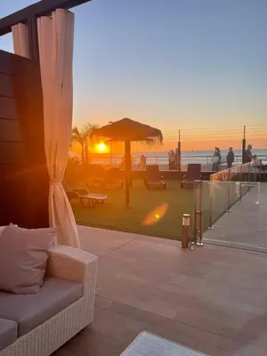a living room with a couch on a balcony with the sunset at Apartamento con piscina en el Paseo Cruz del Mar in Chipiona