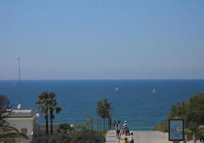 a group of people walking on a sidewalk near the ocean at El Mirador de Inés - Primera Línea de Playa in El Puerto de Santa María