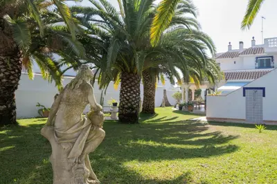 a statue of a woman holding a child in front of palm trees at Villa La Contenta jardín y piscina en Conil centro in Conil de la Frontera