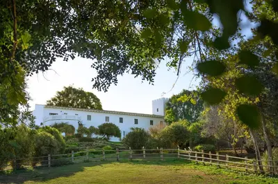a white building with a fence in front of a yard at Cortijo de Guerra in Puerto Real