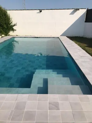 a swimming pool with a tile floor and a white wall at las camelias in El Puerto de Santa María