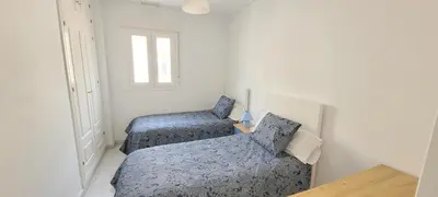 two twin beds in a white room with a window at Casa Playa de Valdelagrana in El Puerto de Santa María