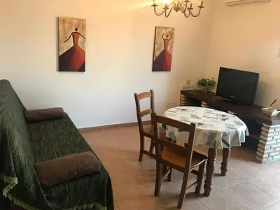 a living room with a table and a chair and a television at Conil, Colorado 2 rustico y económico in Conil de la Frontera